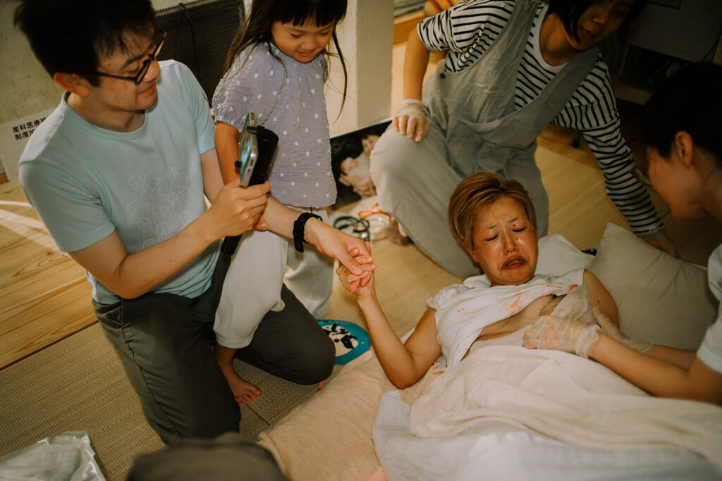 赤ちゃんが産まれてすぐに抱きかかえて涙を流すお母さんと、それを見守るお父さんと長女。